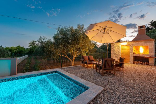 Vila za odmor s bazenom u Hrvatskoj, noćno osvjetljenje bazena i drveni stol sa stolicama i suncobranom