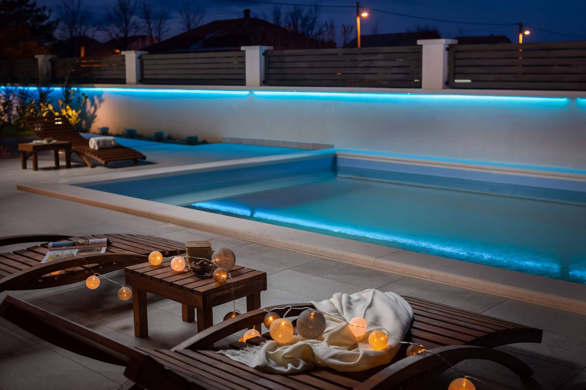 Swimmingpool mit nachtblauer Beleuchtung und Liegestühlen